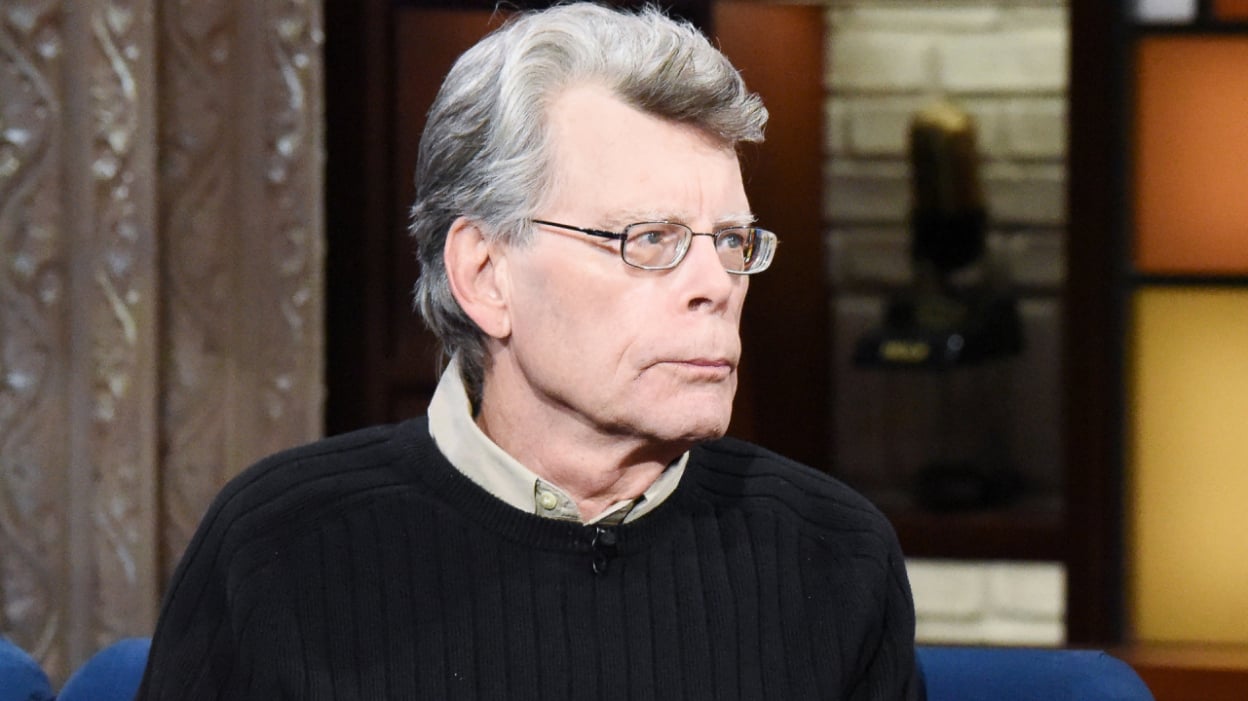 A man with glasses sits on a talks show sofa.