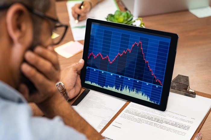 A visibly concerned person looking at a rapidly rising then tumbling stock chart on a tablet.