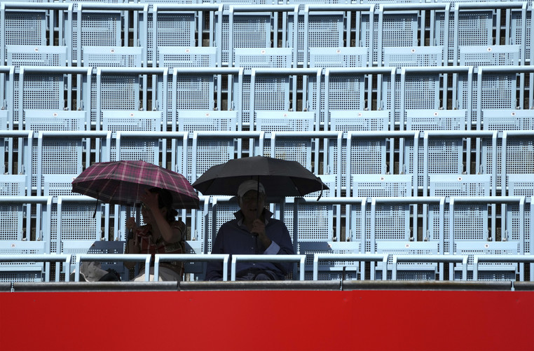 Two people hold umbrellas as they attend the WTA tournament semifinal tennis match.