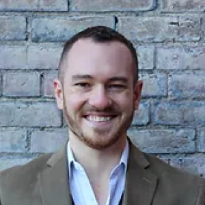 Headshot of Lecturer in Finance Chase Cichetti, wearing a white oxford shirt and taupe blazer